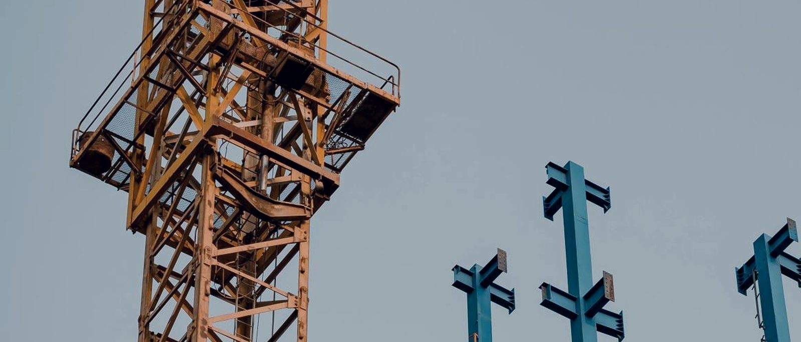 Fabricated steel columns with cruciform brackets standing against the sky beside a tower crane